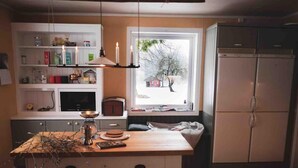 A kitchen with a wooden island, white cabinets, a window with a view of a snowy landscape, and a refrigerator.