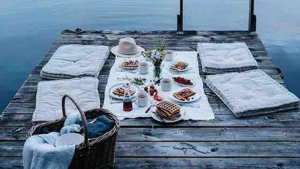 A wooden dock with a picnic setup featuring waffles, a basket, and a hat.