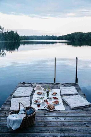 A wooden dock with a picnic setup featuring waffles, a basket, and a hat. - Charming 6 Bedroom House & Horse Farm - Sleeps 12 (Horndal)
