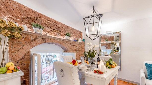 A dining area with a brick wall, a hanging light fixture, and a table set with fruits and a candle.