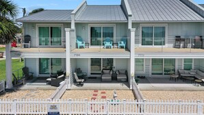 A two-story building with a covered patio area featuring outdoor seating, a white picket fence, and a sign indicating the property is for sale. - Pet Friendly, Ground Floor TH with  Gulf Views ~ Mimi's Place (St. Joe Beach)