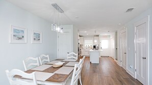 A dining area with a wooden table and white chairs, a kitchen in the background, and a hallway leading to a door labeled "DRESS". - Pet Friendly, Ground Floor TH with  Gulf Views ~ Mimi's Place (St. Joe Beach)