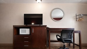 A hotel room with a wooden desk, a television, a microwave, a round mirror, and a chair. - Kings Inn Motel (Reading)