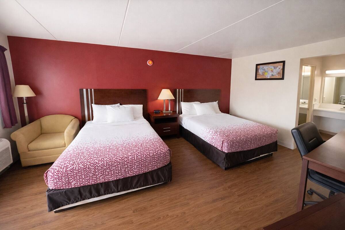 A hotel room with two beds, a chair, a desk, and a mirror.