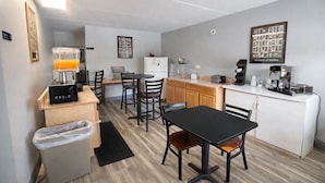 A compact kitchen with a coffee machine, a refrigerator, and a dining area with chairs and a table. - Kings Inn Motel (Reading)