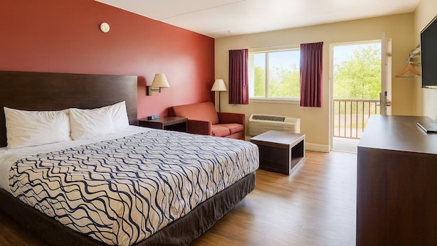 A hotel room with a large bed, a desk, a chair, a TV, and a window with curtains. - Kings Inn Motel (Reading)