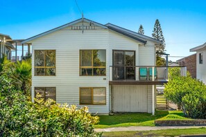 Stunning two-story home with a gabled roof and inviting front porch, featuring large windows and a garage door, set amidst beautifully maintained lawns and lush greenery.