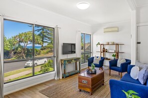 Relax in this stylish living room with a view of the coastal landscape, featuring a comfortable sofa, flat-screen TV, and wooden coffee table.