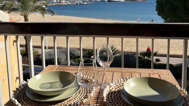 A wooden deck with a table set for two, overlooking a marina with boats and a distant island. - Appartement en face de la plage *** / Apartment with beach view *** (Sainte-Maxime)