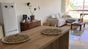 A modern kitchen with a wooden island, a white refrigerator, and a dining area with a sofa and a coffee table. - Appartement en face de la plage *** / Apartment with beach view *** (Sainte-Maxime)