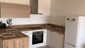 A modern kitchen with a wooden island, built-in oven, stainless steel range hood, and a white refrigerator. - Appartement en face de la plage *** / Apartment with beach view *** (Sainte-Maxime)