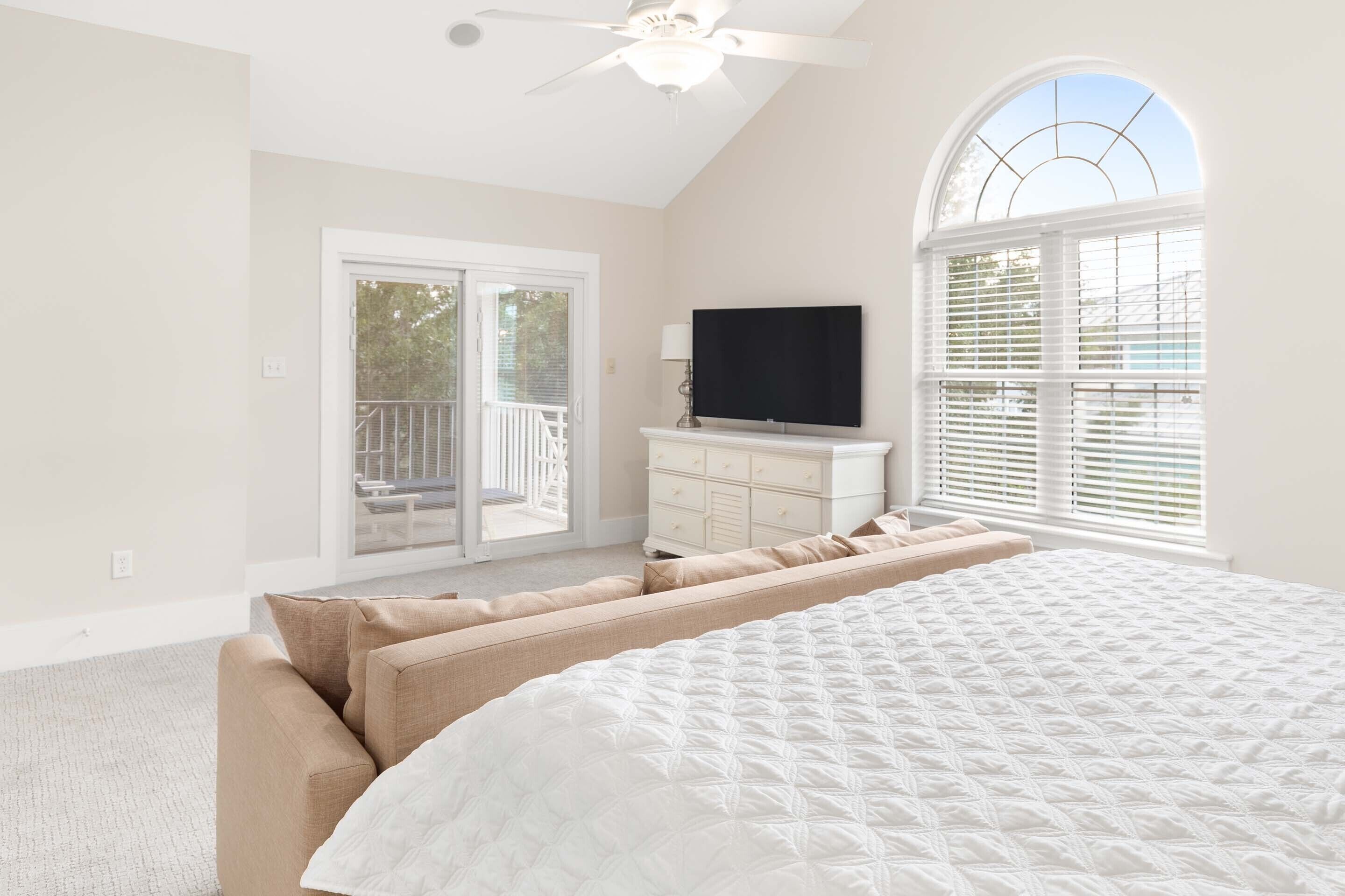 A bedroom with a large bed, a TV, a dresser, and a balcony.