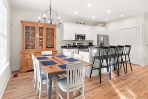 Una cocina moderna con armarios blancos, una mesa de comedor de madera y una lámpara de araña.