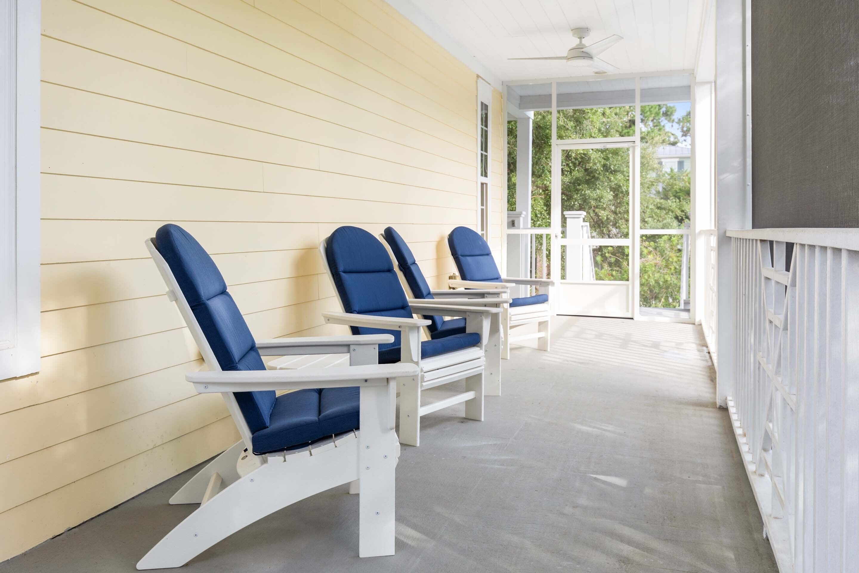 A covered porch with three Adirondack chairs and a table.