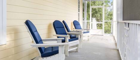 A covered porch with three Adirondack chairs and a table.