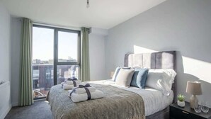 Et moderne hotelværelse med en stor seng, et natbord, en lampe og udsigt over byen fra vinduet.