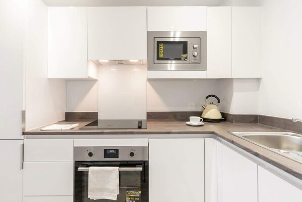 A modern kitchen with white cabinets, a built-in microwave, a kettle, and a stainless steel sink.