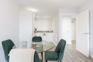 A modern kitchen with white cabinets, a countertop, and a dining area with a glass table and green chairs.