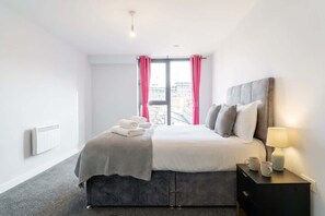 A modern hotel room with a bed, bedside table, and a window with curtains.