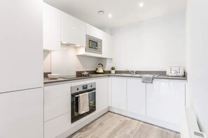 Una cocina moderna con armarios blancos, un microondas, un horno y un lavamanos.
