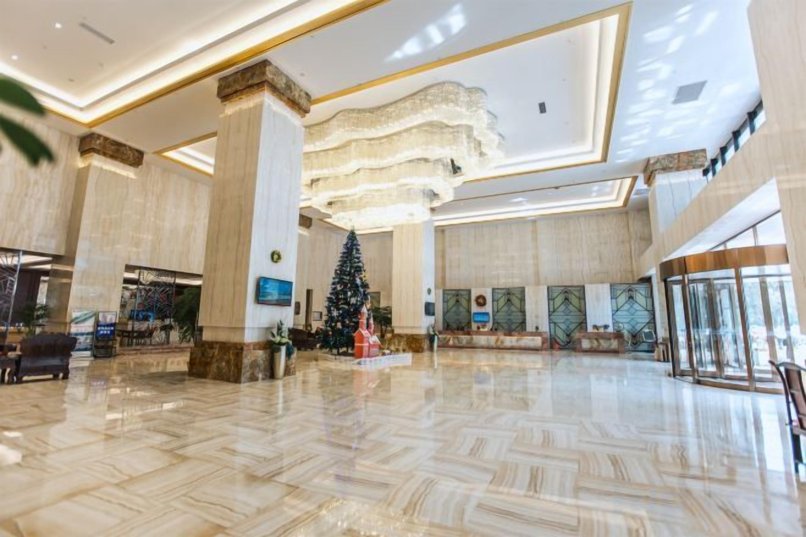 A spacious lobby with a large Christmas tree, marble flooring, and a modern chandelier.