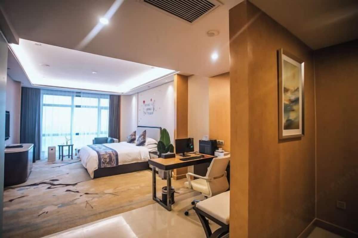 Habitación de hotel con cama, escritorio, silla y un amplio ventanal.