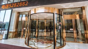 A hotel entrance with a revolving door, glass doors, and a contact number above.