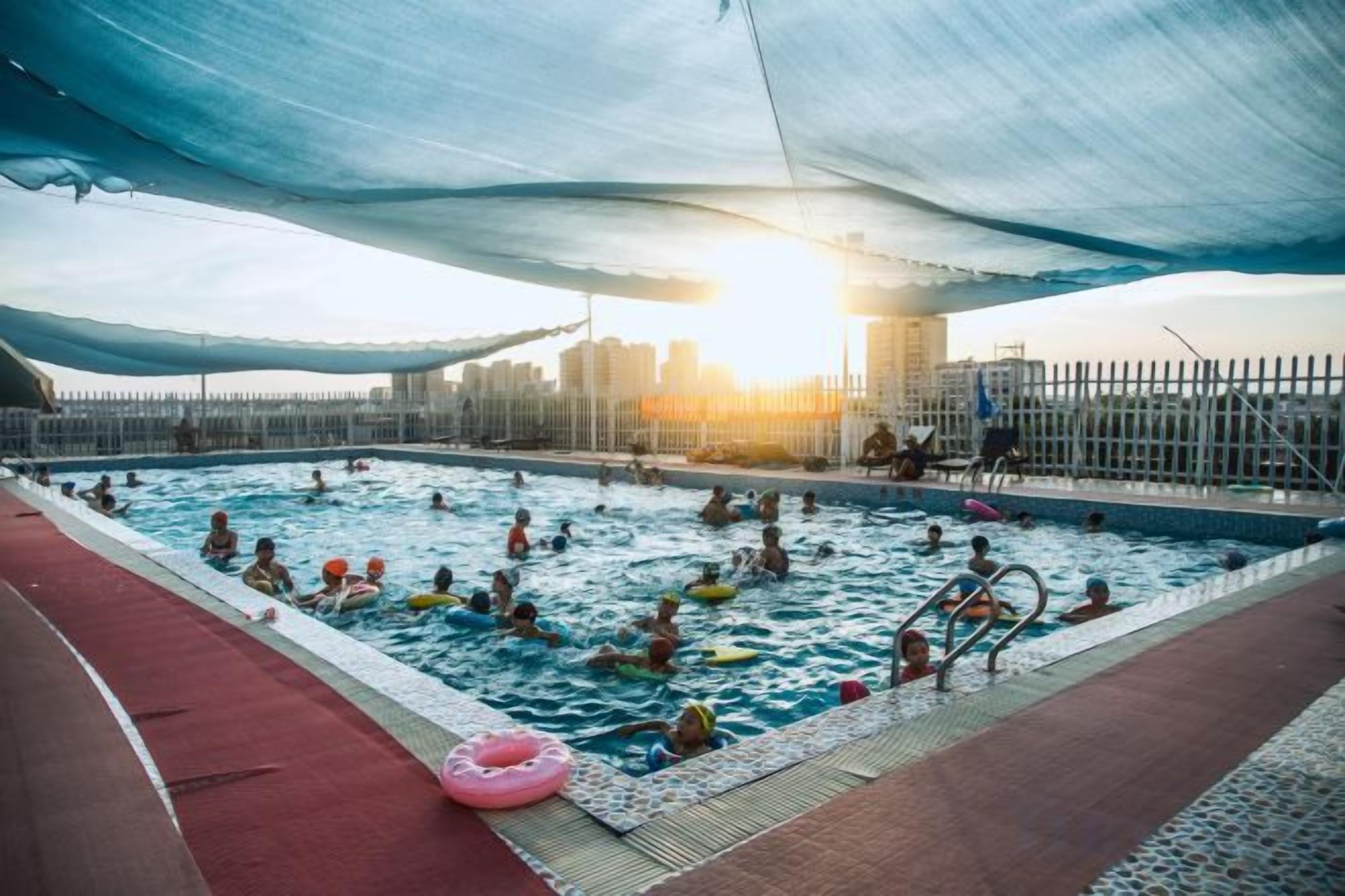 Una piscina interior con varias pistas de natación, una pista de atletismo roja y una vista panorámica de la ciudad al fondo.