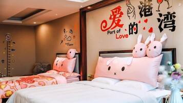 A hotel room with two beds, each with pink bedding and a bunny-themed pillow. A wall decoration reads "Port of Love" with illustrations of hearts and wine glasses.