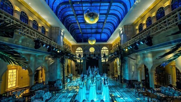 A grand hall with a central fountain, ornate architecture, and a starry ceiling.