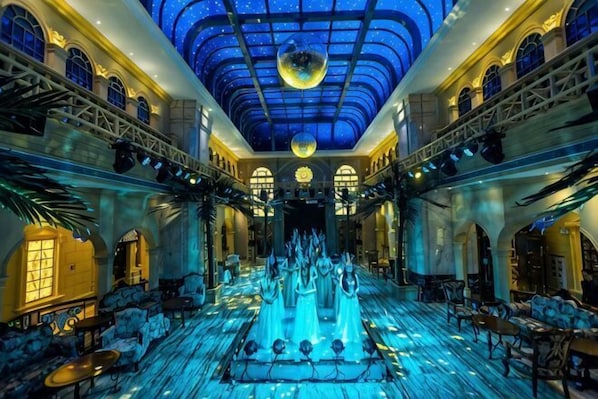 A grand hall with a central fountain, ornate architecture, and a starry ceiling.