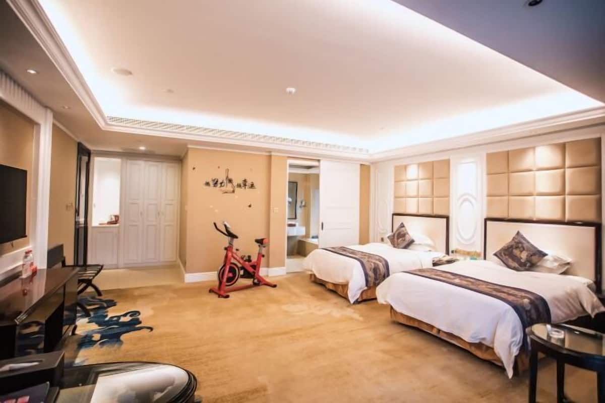 Habitación de hotel con dos camas, televisión, escritorio y bicicleta estática.