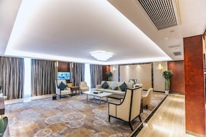 A modern hotel lobby with a sofa, chairs, a coffee table, a TV, and a patterned carpet.