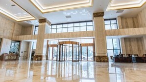 A spacious lobby with marble flooring, large windows, and a revolving door.