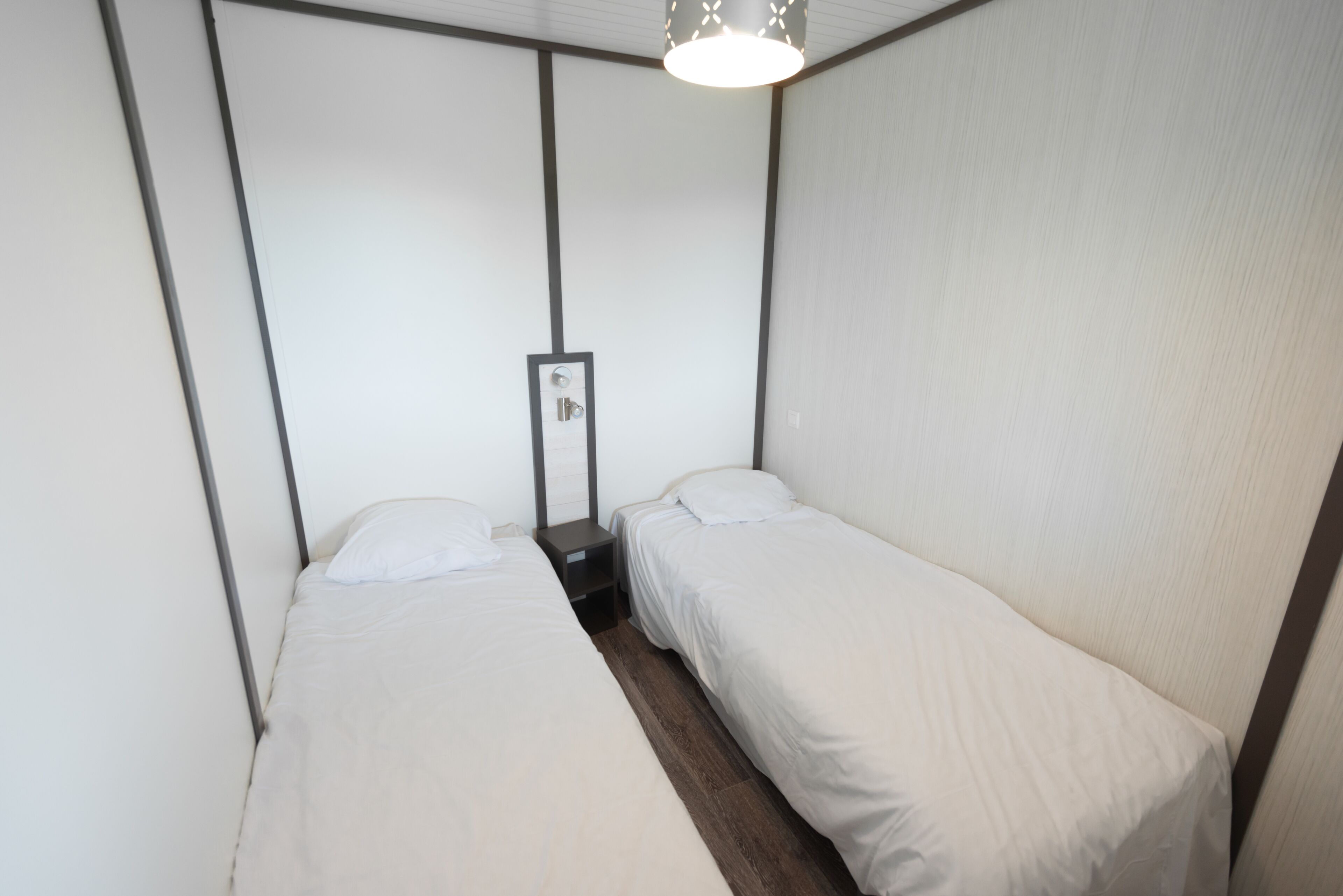 Ein kleines Hotelzimmer mit zwei Einzelbetten, einem Nachttisch und einem Spiegel.