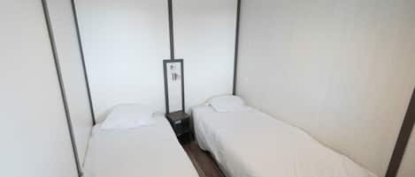 A small, single-room hotel room with two single beds, a nightstand, and a mirror.