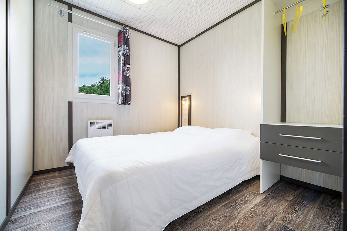 A modern bedroom with a bed, a dresser, a window with a view, and a ceiling fan.