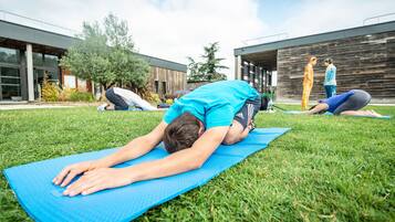 Une personne effectue une posture de yoga sur un tapis bleu, dans un cadre extérieur, avec des bâtiments en arrière-plan.