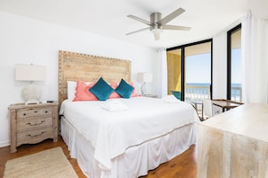A bedroom with a bed, bedside tables, a ceiling fan, a view of the sea, and a balcony.