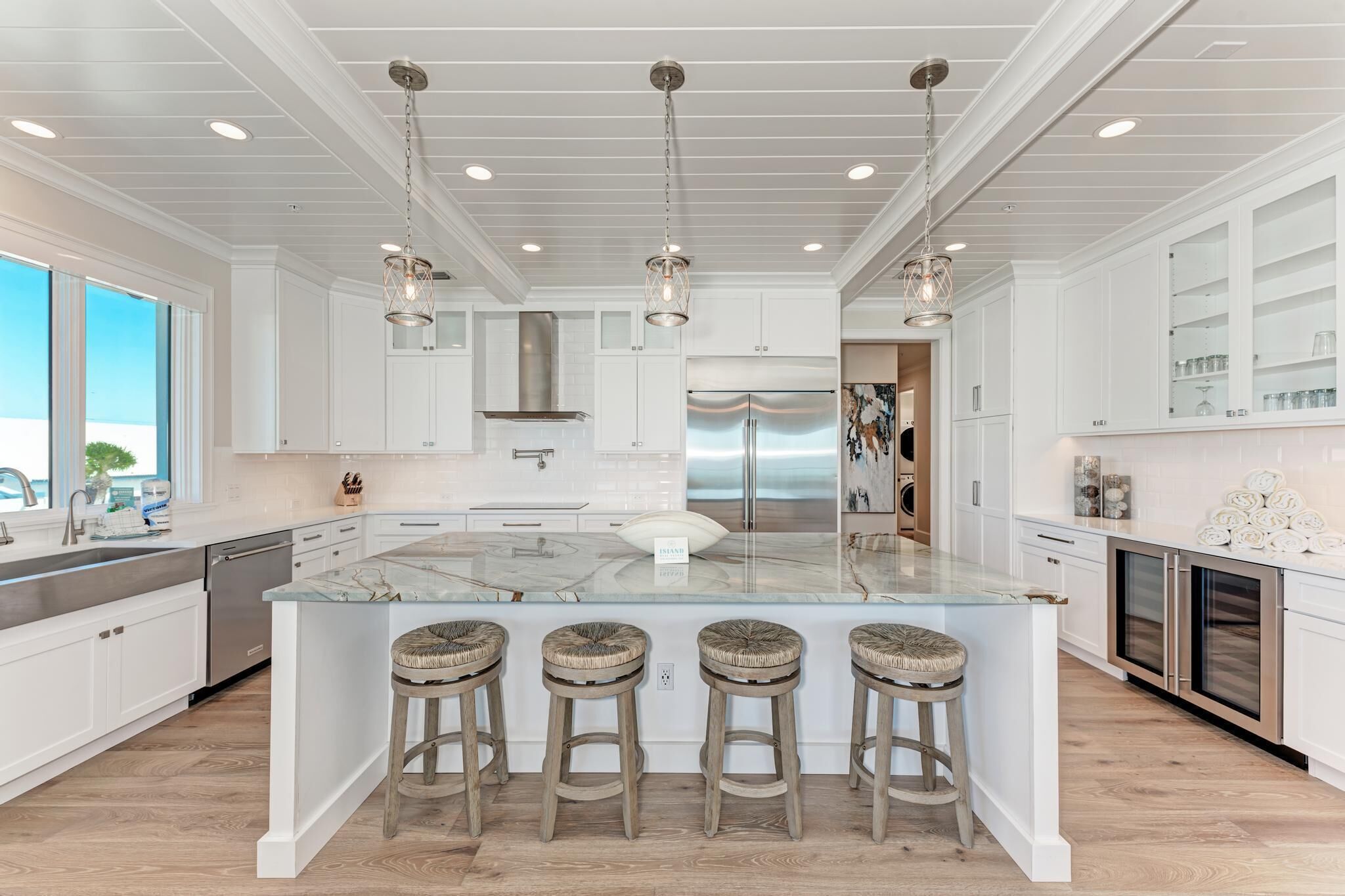A modern kitchen with white cabinetry, a large island with bar stools, stainless steel appliances, and pendant lighting.