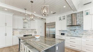 A modern kitchen with white cabinetry, a large island with bar stools, stainless steel appliances, and a unique backsplash.