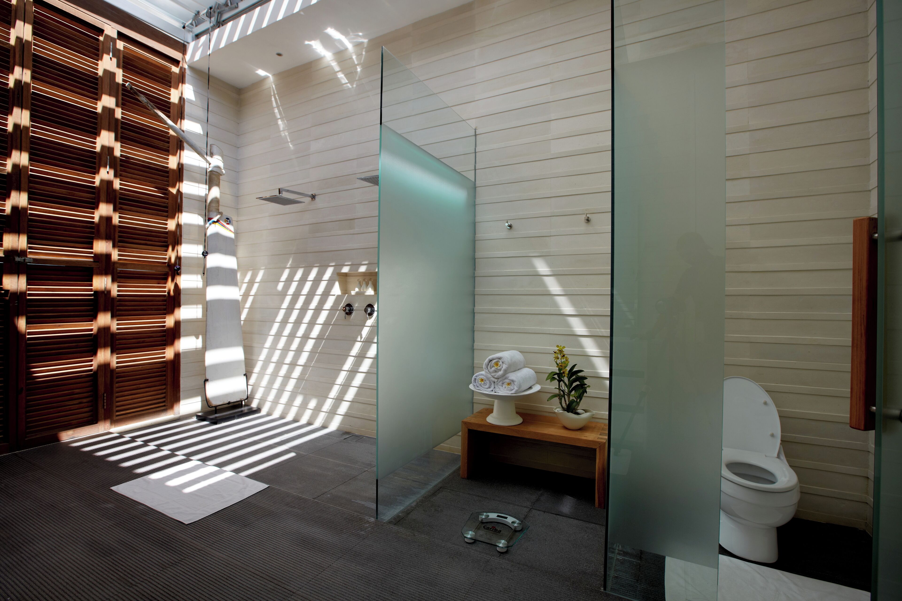 A modern bathroom with a glass partition, a wooden bench, a toilet, and a shower area.