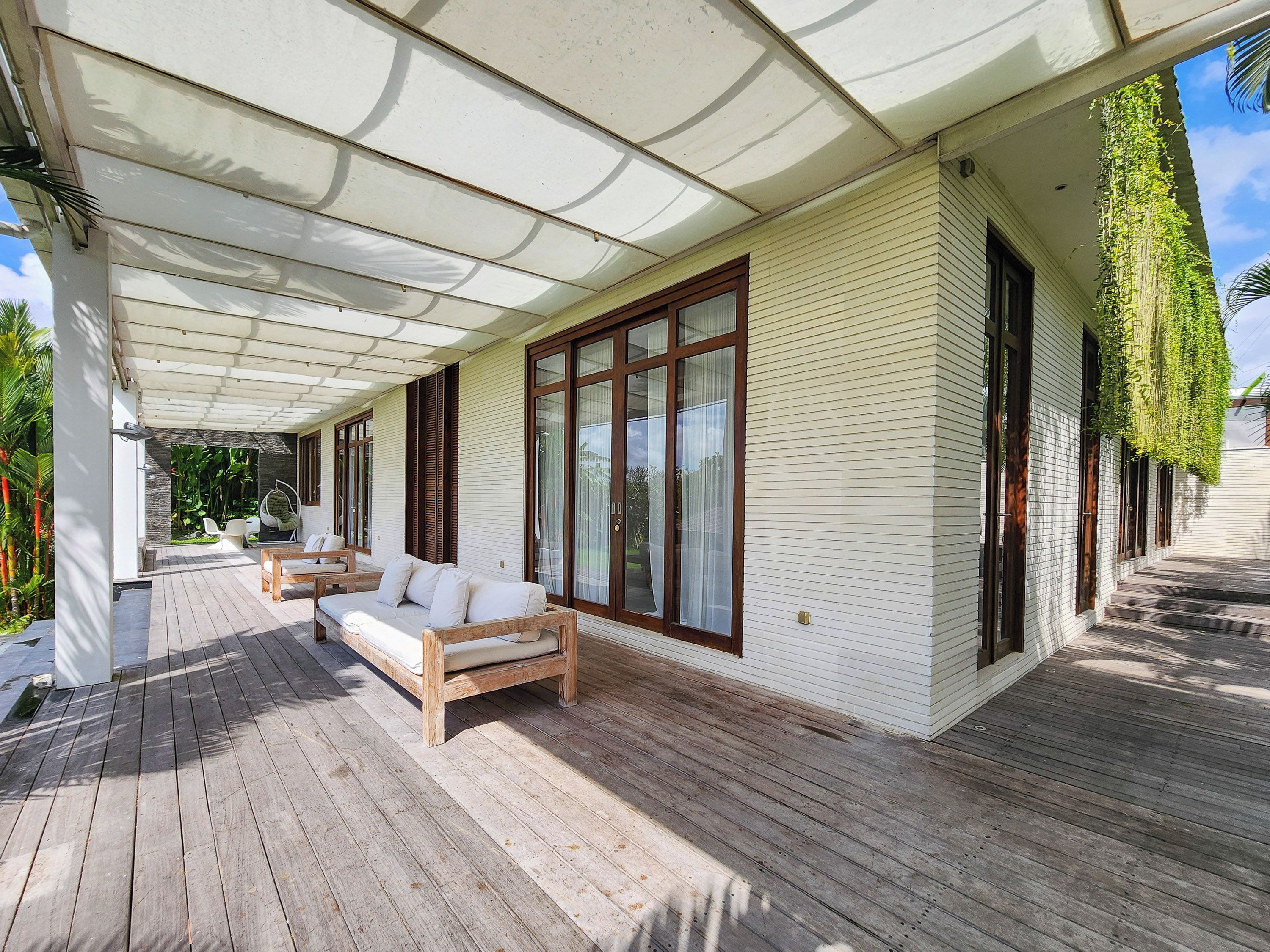 Un espacio exterior techado con una terraza de madera, un sofá y una mesa de comedor.
