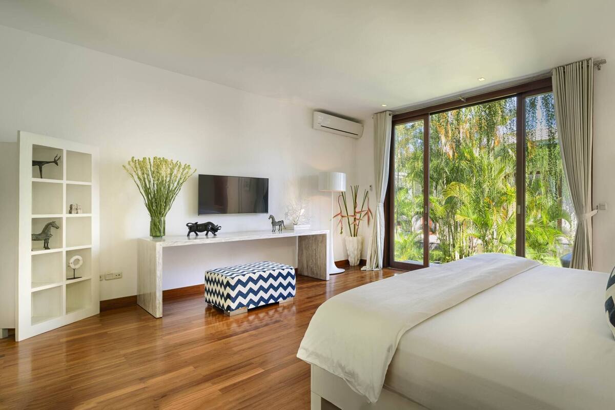 Een moderne slaapkamer met een groot bed, een inbouw bureau, een televisie en uitzicht op groen door het raam.