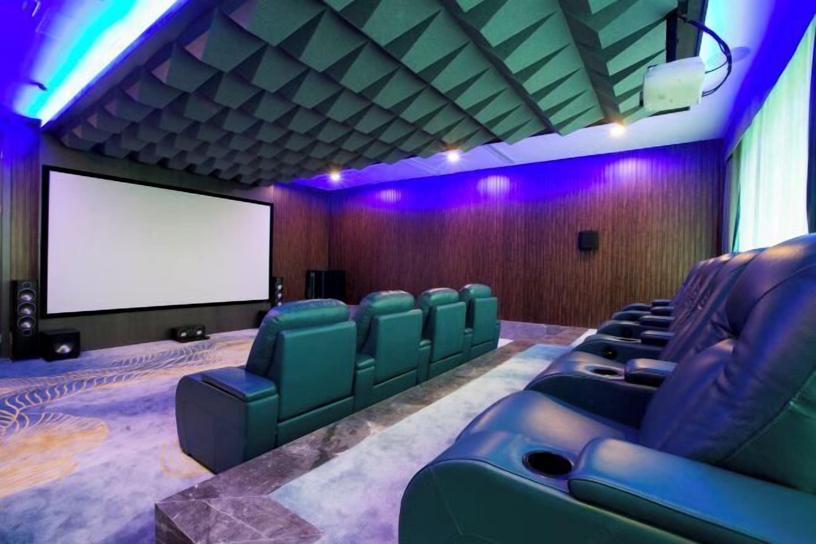 A home theater room with a large screen, green seating, and a projector.