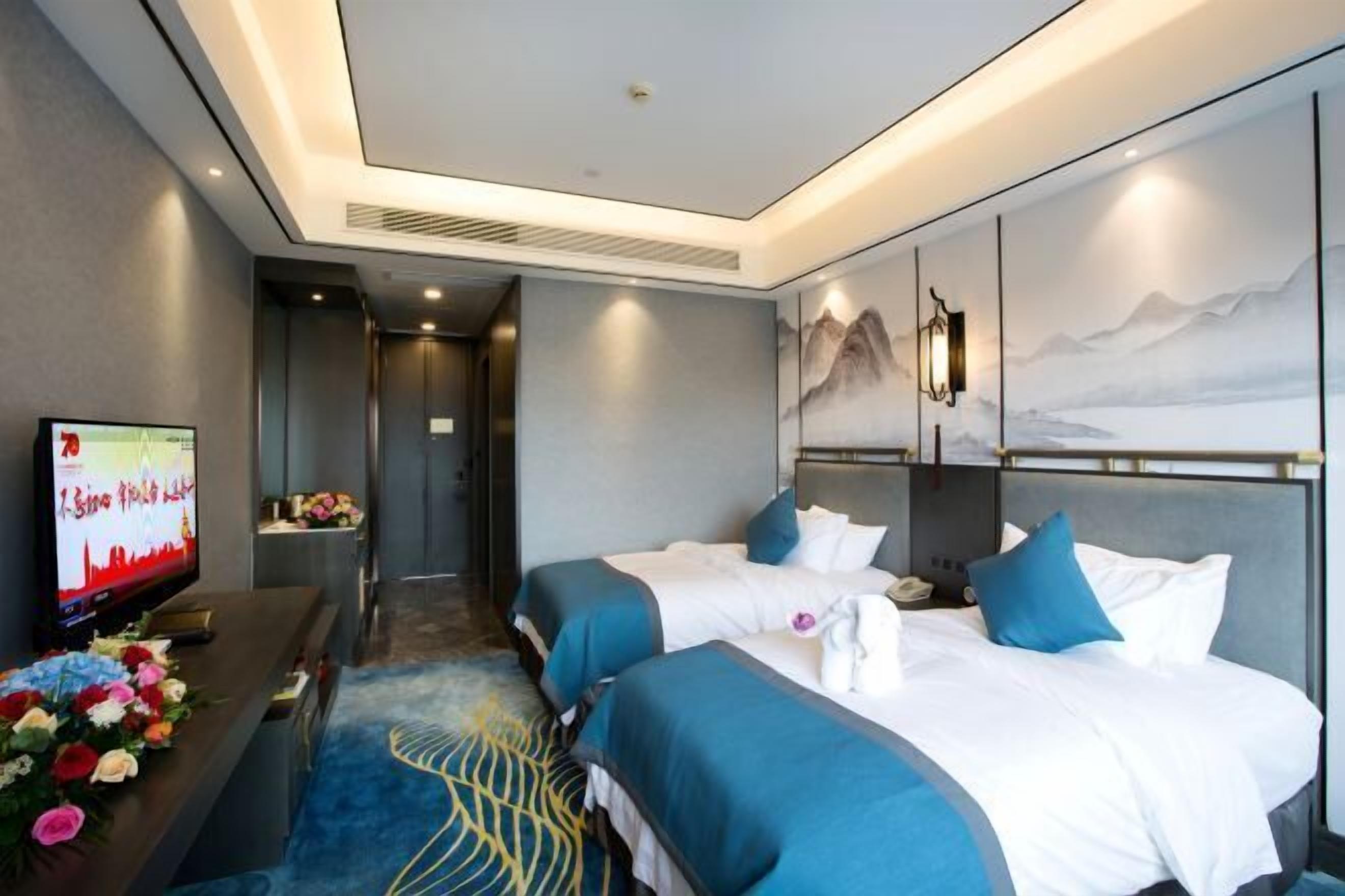 A hotel room with two beds, a TV, a desk, and a wall with a mountain painting.