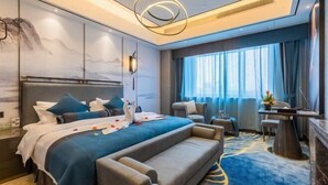 A modern hotel room with a large bed, a sofa, a desk, and a view of the city through large windows. - Yangzi International Hotel (Liyang)