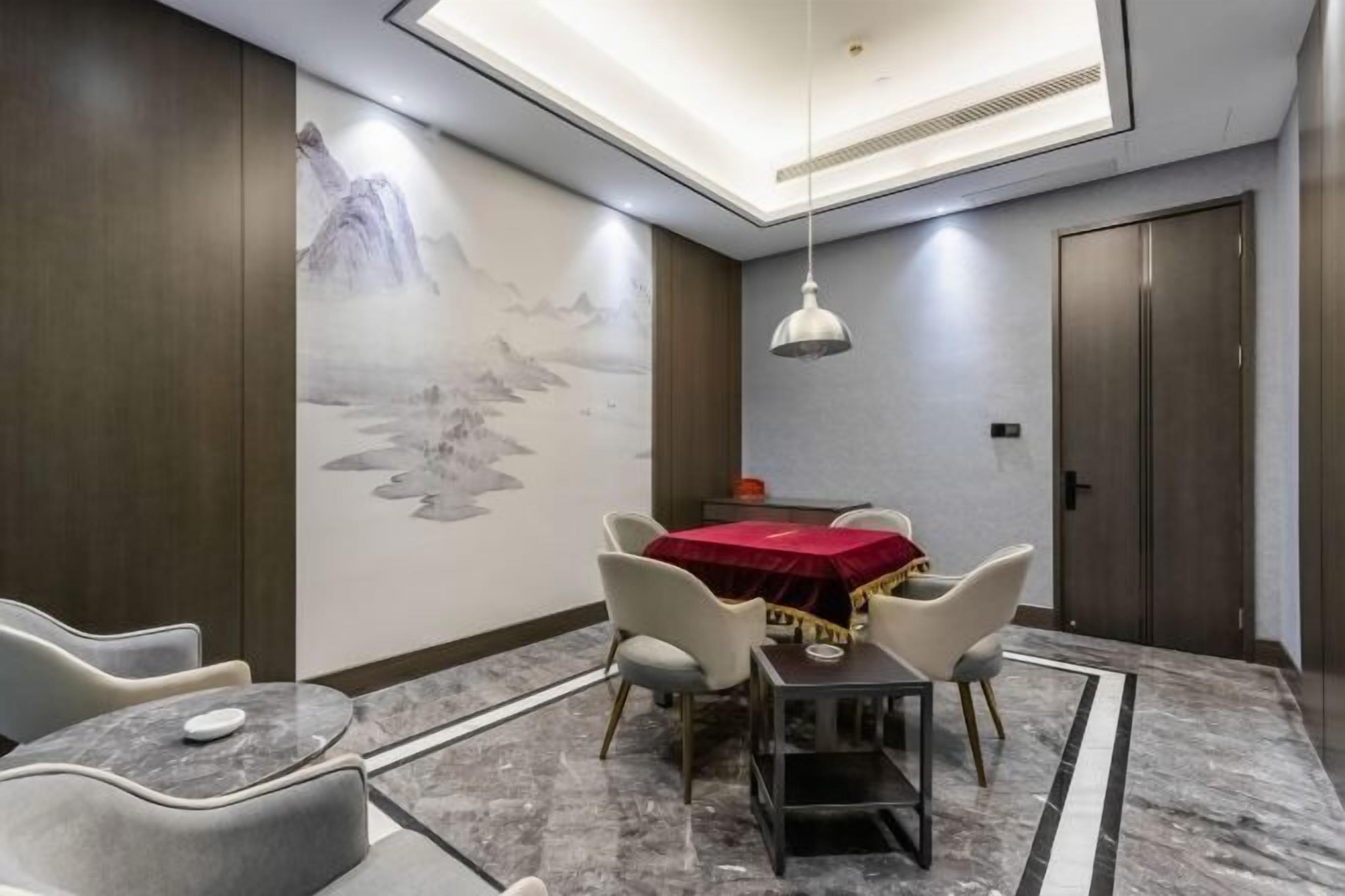 Un comedor con una mesa cubierta por un mantel rojo, rodeado de sillas y un mural en la pared.