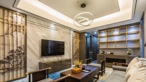 A modern living room with a flat-screen TV, a sofa, a coffee table, and a bookshelf. - Yangzi International Hotel (Liyang)