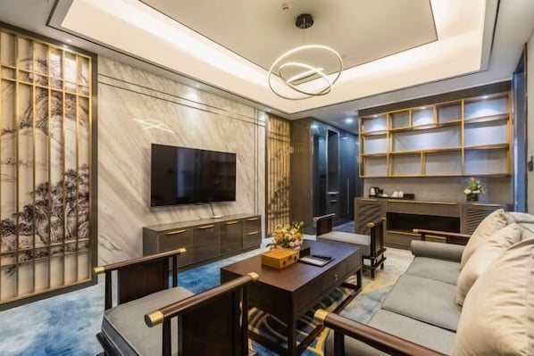 A modern living room with a flat-screen TV, a sofa, a coffee table, and a bookshelf. - Yangzi International Hotel (Liyang)